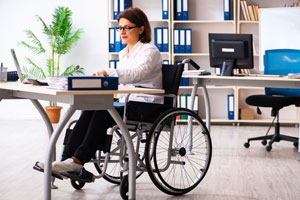 Büroarbeitsplatz: Frau im Rollstuhl sitzt vor Schreibtisch 