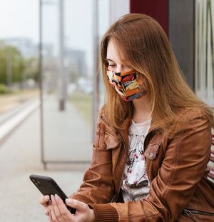 Femme avec masque barrière sur une plate-forme, regardant son téléphone portable.