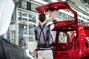 Fabrikarbeiter montiert, unterstützt von einem Exoskelett, eine PKW-Heckklappe