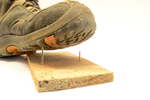 Arbeitsschuh tritt auf Holzbrett mit Nagel