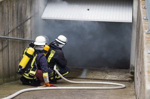 Feuerwehrmänner in Schutzausrüstung vor Garage aus der Rauch dringt