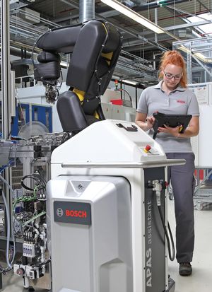 APAS, kollaborierender Roboter der Firma Bosch, im Hintergrund bedient eine Mitarbeiterin ein Tablet
