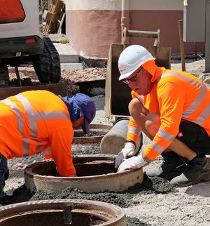 Deux ouvriers du bâtiment travaillant en extérieur portant des vêtements de protection et couvre-chefs