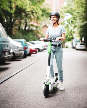 Junge Frau mit Helm fährt mit einem E-Scooter auf der Straße