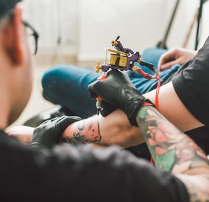 Tattooist with protective gloves tattoos the forearm of a customer.