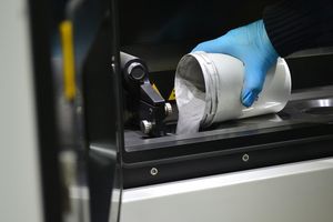 Un homme verse de la poudre de métal dans la chambre d'une machine de frittage laser, une imprimante 3D qui imprime des pièces métalliques.