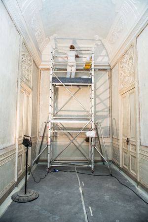 A restorer is standing on a mobile scaffold and working on a stucco ceiling