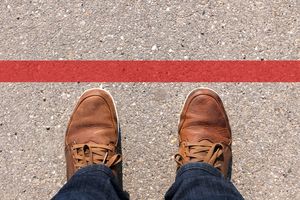 Zwei Füße vor einer auf den Asphalt aufgemalten roten Linie