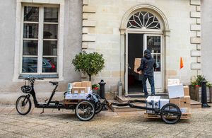 Ein mit Paketen bepacktes Lastenrad mit Anhänger steht vor einem Haus, Kurier liefert Paket aus