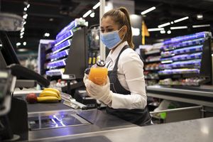 Verkäuferin mit medizinischer Maske an einer Supermarktkasse