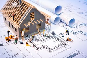 Model construction of a house in shell, standing on a construction drawing and with small construction worker figures working on it