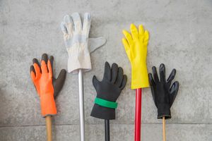 Fünf verschiedene Schutzhandschuhe auf Besenstielen vor einer Wand