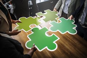Plusieurs personnes réunissent quatre grandes pièces de puzzle vertes.