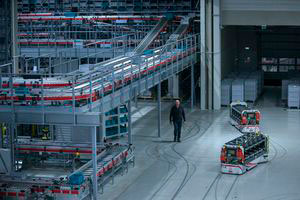Deux grands chariots de transport sans conducteur circulent dans un entrepôt. Une personne marche à proximité.