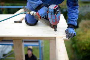 Handwerker, der mit einer Bohrmaschine ein Loch in eine Holzplatte bohrt.