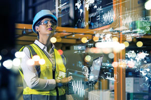 Eine Beschäftigte in Sicherheitskleidung sieht durch eine Sicherheitsbrille in eine durch augmented reality vernetzte Arbeitswelt 