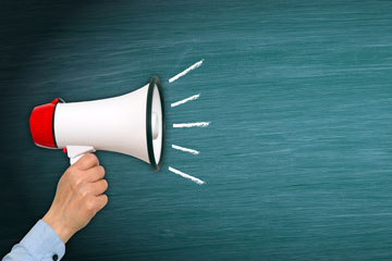 Eine Person hält vor einer grünen Tafel ein Megafon in der Hand.. Click opens the page European Commission presents 2025 work programme for European standardisation