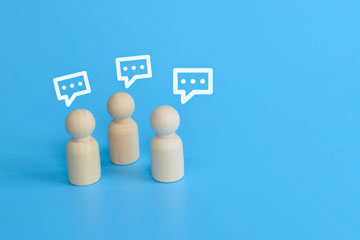 Holzpuppenfiguren mit symbolisierten Sprechblasen. Klick öffnet die Seite DGUV Barometer 2025: Wie sicher und gesund ist unsere Arbeitswelt?