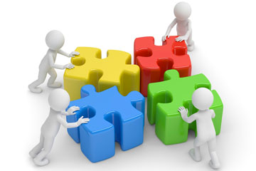 Vier stilisierte Figuren, die jede ein verschieden farbiges Puzzleteil vor sich her zu einem Ganzen zusammenschiebt.. Klick öffnet die Seite KAN-Fachgespräch „Advanced Materials und Arbeitsschutz“ 2025 