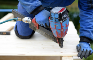 Handwerker, der mit einer Bohrmaschine ein Loch in eine Holzplatte bohrt.