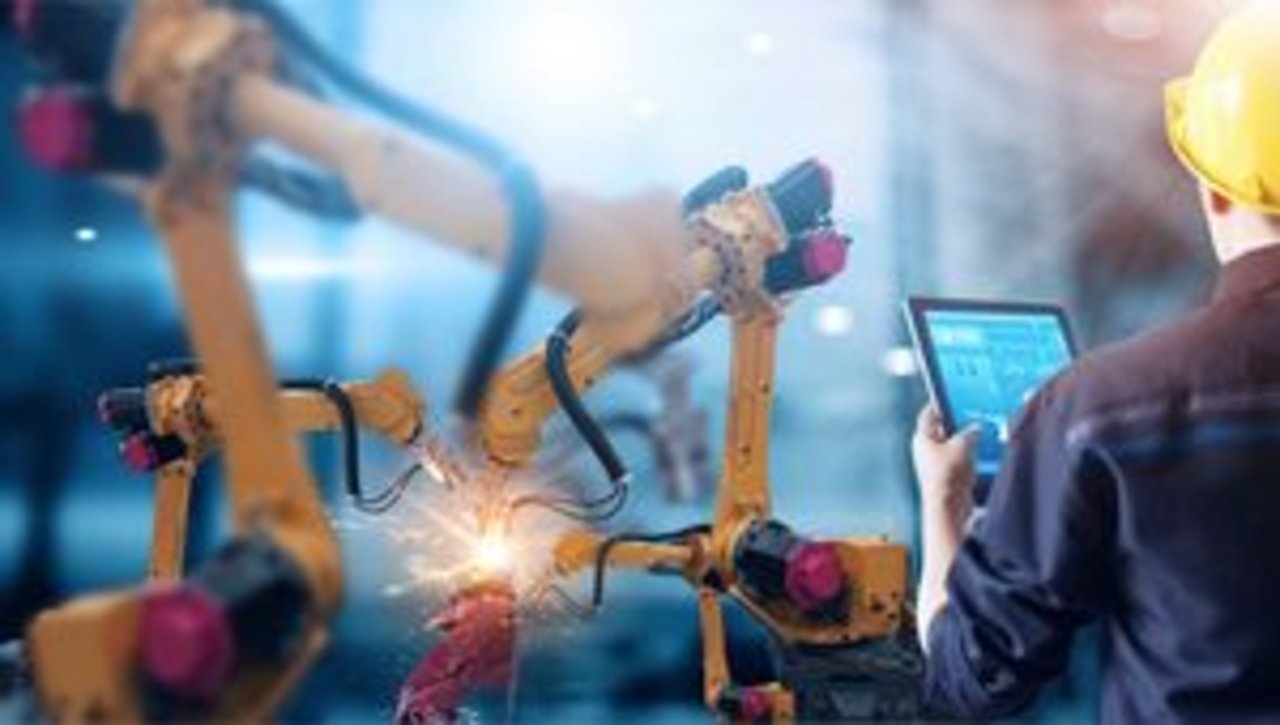 Un ingénieur surveille sur sa tablette les bras robotiques de soudage dans une usine intelligente.