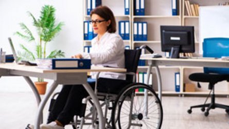 Büroarbeitsplatz: Frau im Rollstuhl sitzt vor Schreibtisch 