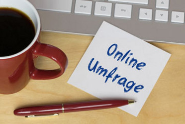 Neben einer Kaffeetasse, einer Tastatur und einem Kugelschreiber liegt ein Zettel mit dem Hinweis Online-Umfrage.