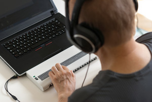 Mann mit Kopfhörern arbeitet an einem Laptop mit Braille-Zeile 