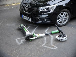 Accident scene with an electric kick scooter and a helmet lying in front of a car.