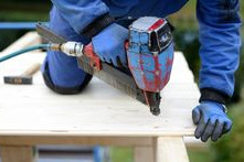 Handwerker, der mit einer Bohrmaschine ein Loch in eine Holzplatte bohrt.