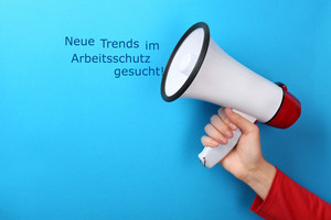 Eine Frau hält ein Megafon in der Hand und verkündet, dass neue Trends im Arbeitsschutz gesucht werden.