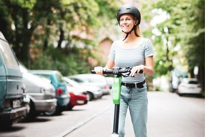 Junge Frau mit Helm fährt mit einem E-Scooter auf der Straße