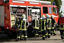Gruppe von Feuerwehrleuten in Schutzkleidung und mit Helm entlädt Ausrüstung von einem Feuerwehrfahrzeug