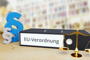 Ordner auf Schreibtisch mit Beschriftung "EU-Verordnung" neben Paragraf und Waage.
