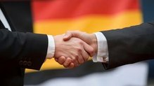 Zwei Menschen geben sich die Hand, im Hintergrund eine deutsche Flagge
