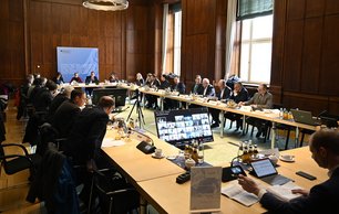 Mehrere Menschen sitzen an einem Tisch, in einem Besprechungssaal 