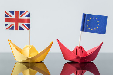 Zwei Papierschiffe, eines mit britischer und eines mit europäischer Flagge auf einer glänzenden Tischplatte