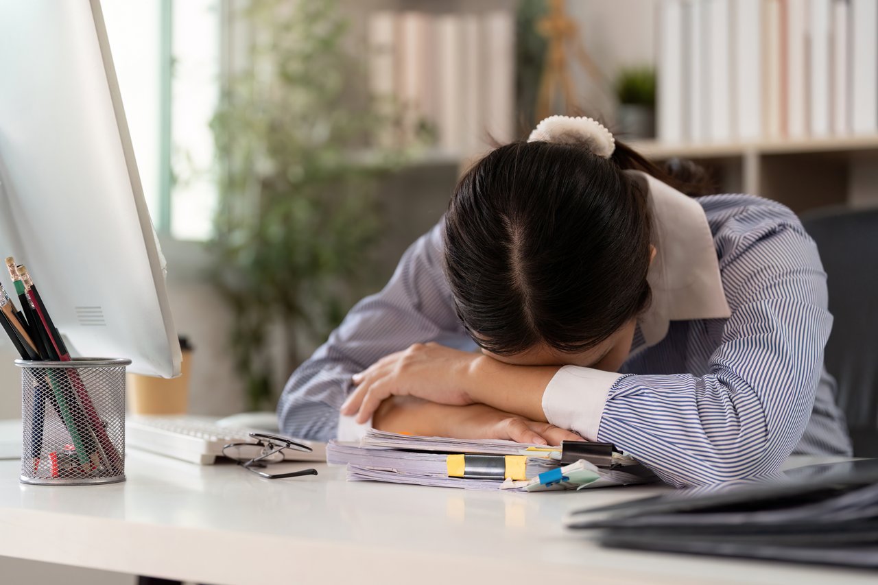 Junge Frau, die ihren Kopf auf Papierdokumenten auf dem Schreibtisch gelegt hat