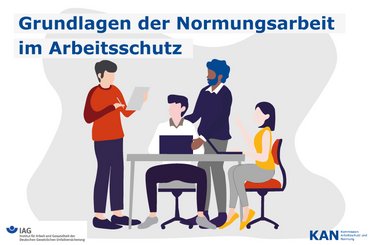 Drei Seminarteilnehmende sitzen bzw. stehen um einen Schreibtisch mit Laptop und schauen auf einen Dozenten.herum. Click opens the page KAN seminar on the principles of standardization work
