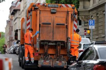 Zwei Müllwerker fahren auf den Trittbrettern eines Abfahrsammelfahrzeugs mit.