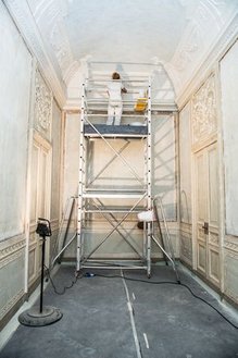 A restorer is standing on a mobile scaffold and working on a stucco ceiling