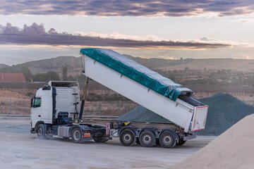 Kipplaster mit einem Kippauflieger, der Kies in einem Steinbruch entlädt, wobei die Kippvorrichtung noch angehoben ist. 