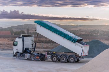 Kipplaster mit einem Kippauflieger, der Kies in einem Steinbruch entlädt, wobei die Kippvorrichtung noch angehoben ist. . Klick öffnet die Seite Experten gesucht: Neue Normen für maschinelle Aufbauten auf Nutzfahrzeugen