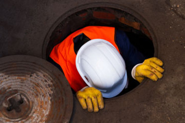 Arbeiter in Schutzkleidung steigt in eine Behälteröffnung.