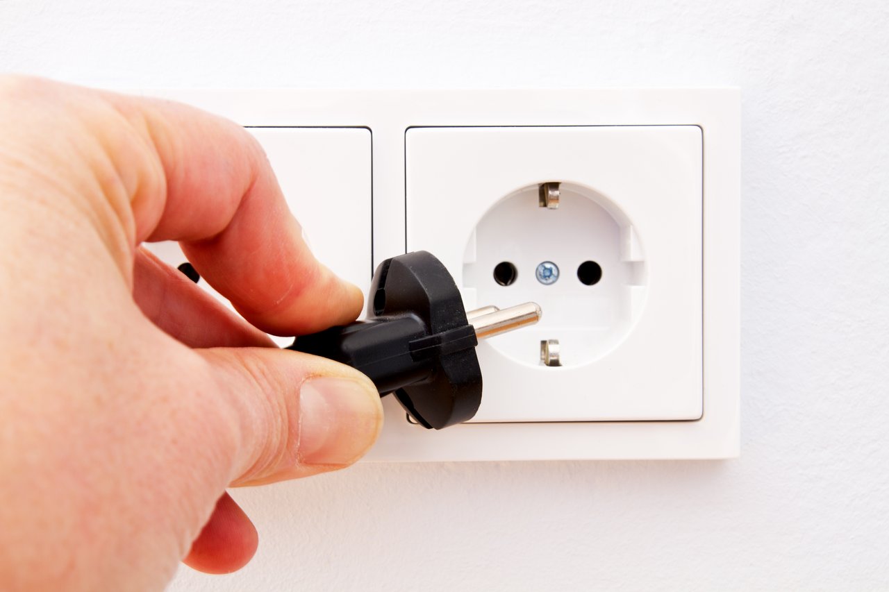 Eine Hand hält einen Stecker vor eine Steckdose in der Wand