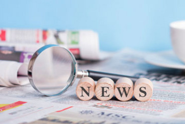 Zeitung und Lupe auf einem Tisch, das Wort "News" steht auf vier Würfeln