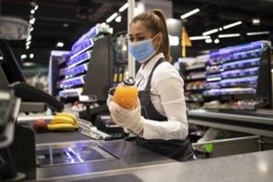 Verkäuferin mit medizinischer Maske an einer Supermarktkasse